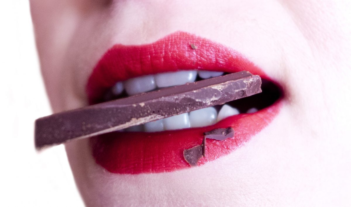 Woman wearing red lipstick biting a piece of chocolate