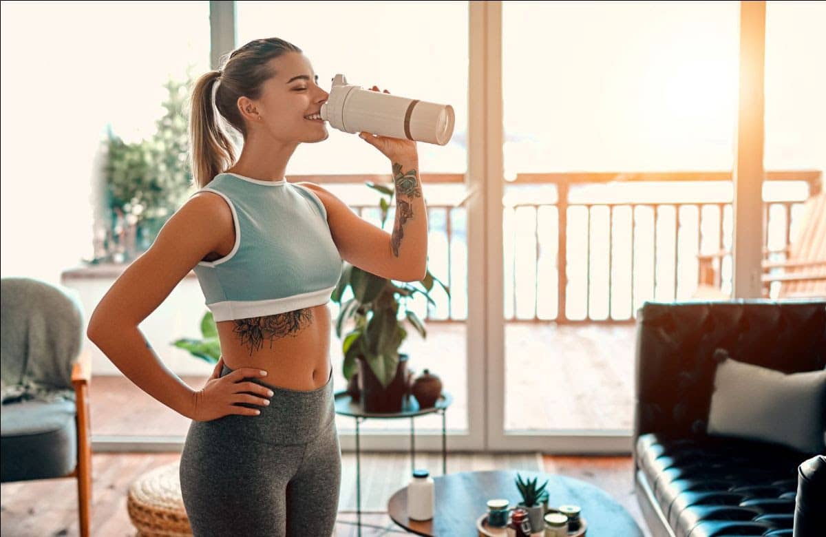 A healthy woman in workout clothing drinking a shake