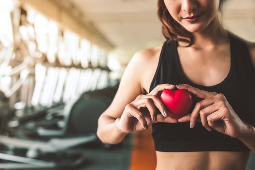A woman in exercise clothing at the gym holding a red heart in front of her chest